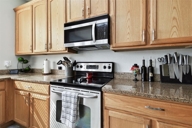 kitchen with light brown cabinetry, stainless steel appliances, and dark stone counters