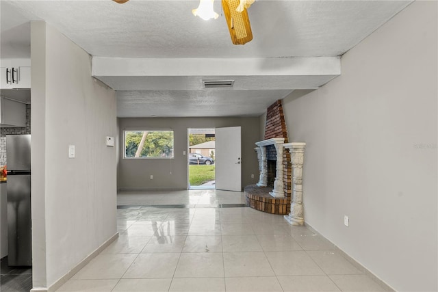 unfurnished living room featuring a textured ceiling, light tile patterned floors, a fireplace, and ceiling fan