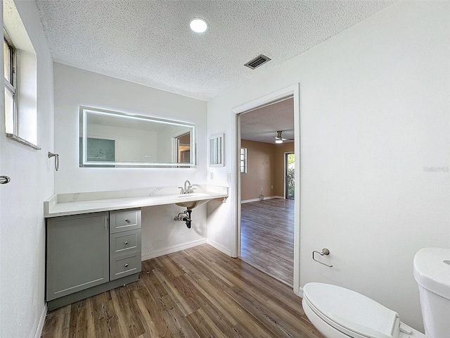 half bathroom featuring toilet, wood finished floors, visible vents, and a textured ceiling