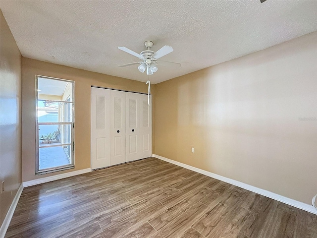 unfurnished bedroom with wood finished floors, baseboards, ceiling fan, a closet, and a textured ceiling