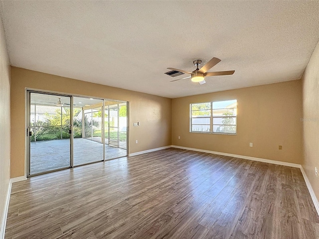 empty room with a textured ceiling, wood finished floors, baseboards, and ceiling fan