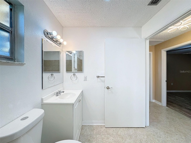 bathroom with baseboards, toilet, vanity, tile patterned floors, and a textured ceiling