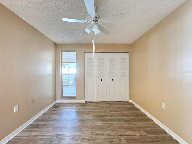 unfurnished bedroom with a closet, a textured ceiling, baseboards, and wood finished floors