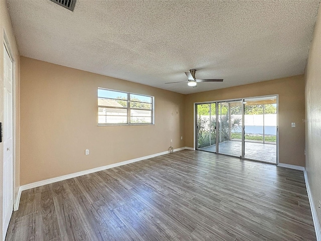 empty room featuring baseboards, a textured ceiling, a ceiling fan, visible vents, and wood finished floors