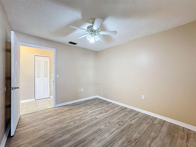 spare room with a textured ceiling, wood finished floors, visible vents, and baseboards