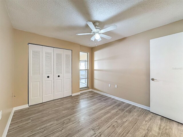 unfurnished bedroom with baseboards, wood finished floors, a closet, a textured ceiling, and a ceiling fan