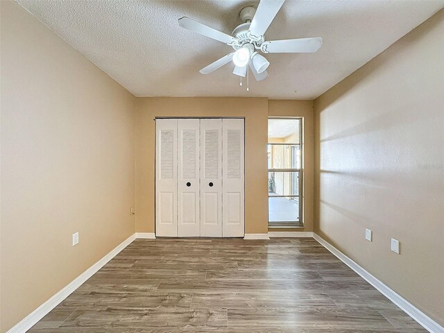 unfurnished bedroom with wood finished floors, baseboards, ceiling fan, a closet, and a textured ceiling