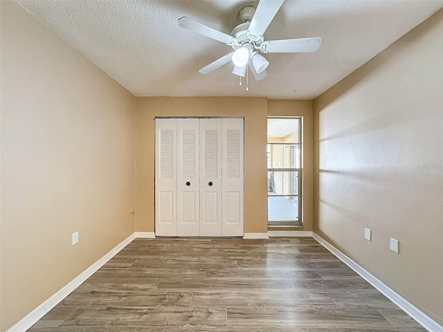 unfurnished bedroom with a closet, baseboards, a textured ceiling, ceiling fan, and wood finished floors