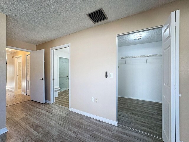 unfurnished bedroom with wood finished floors, baseboards, visible vents, a closet, and a textured ceiling