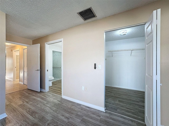 unfurnished bedroom with a textured ceiling, a closet, visible vents, wood finished floors, and baseboards