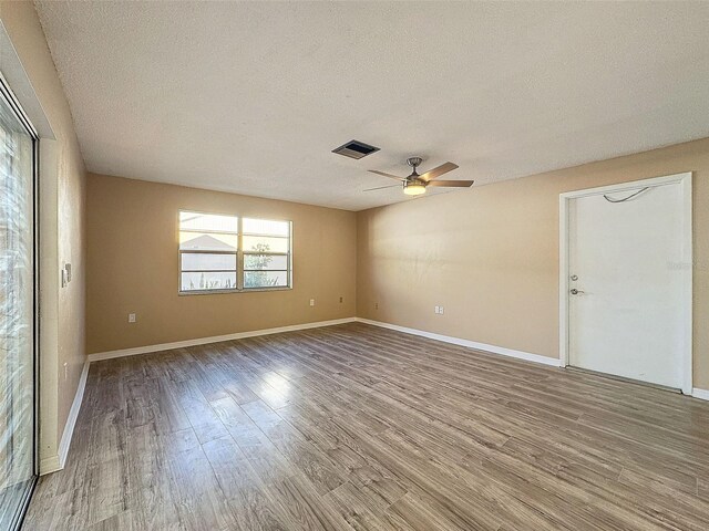 empty room with visible vents, a textured ceiling, wood finished floors, baseboards, and ceiling fan