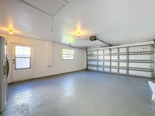 garage featuring stainless steel fridge with ice dispenser, a garage door opener, and concrete block wall