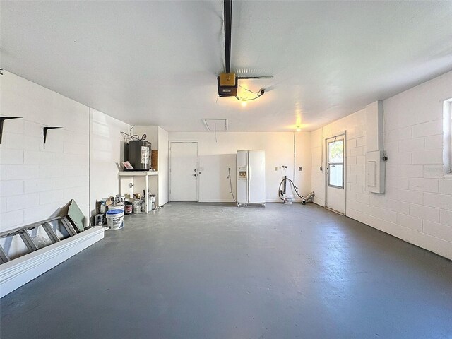 garage featuring water heater, a garage door opener, white refrigerator with ice dispenser, and concrete block wall