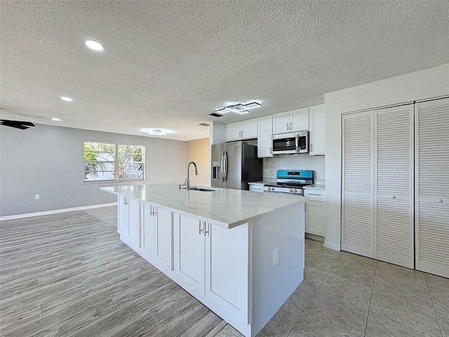 kitchen with a sink, light stone counters, stainless steel appliances, white cabinetry, and a kitchen island with sink