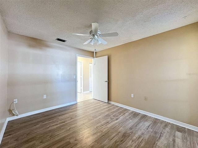 empty room with a textured ceiling, wood finished floors, visible vents, and baseboards