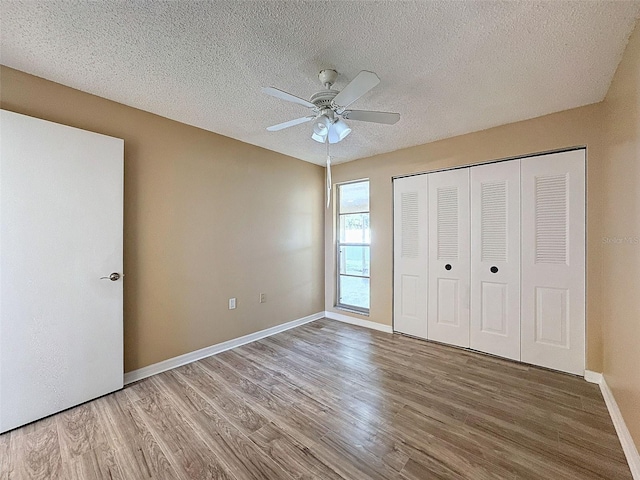 unfurnished bedroom featuring ceiling fan, baseboards, wood finished floors, a closet, and a textured ceiling