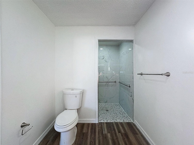 full bath featuring toilet, a textured ceiling, wood finished floors, a tile shower, and baseboards