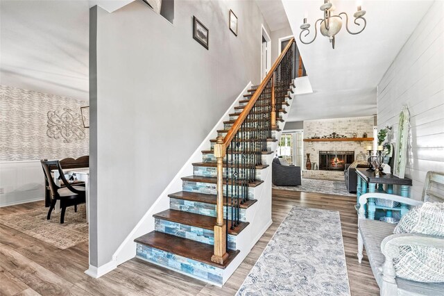 staircase with a towering ceiling, a brick fireplace, hardwood / wood-style floors, and a notable chandelier