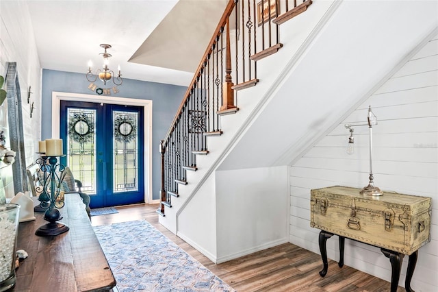 foyer entrance with french doors, wood walls, hardwood / wood-style flooring, and an inviting chandelier