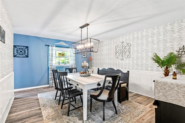 dining room featuring a wainscoted wall, an accent wall, wood finished floors, baseboards, and wallpapered walls