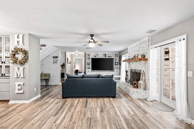 living area with a brick fireplace, ceiling fan, visible vents, and wood finished floors