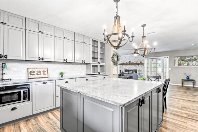 kitchen featuring decorative light fixtures, a brick fireplace, a chandelier, decorative backsplash, and stainless steel microwave