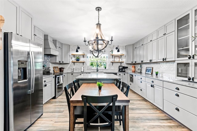 kitchen featuring pendant lighting, custom range hood, a notable chandelier, appliances with stainless steel finishes, and light wood-type flooring