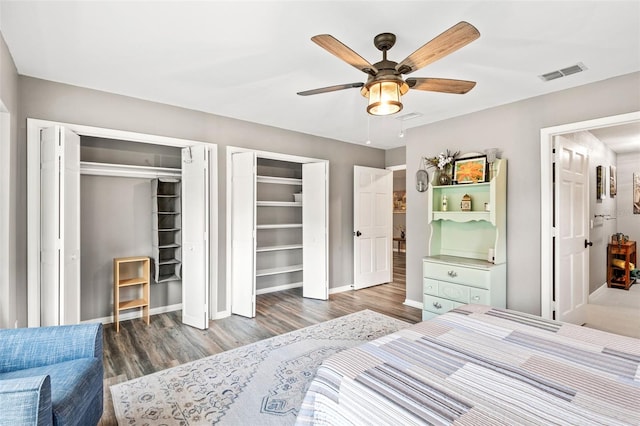 bedroom with ceiling fan, wood finished floors, visible vents, baseboards, and two closets