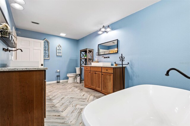 bathroom featuring a tub to relax in, vanity, toilet, and parquet flooring