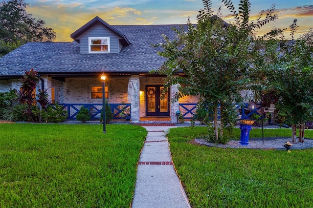 view of front of home featuring covered porch, roof with shingles, a front lawn, and brick siding