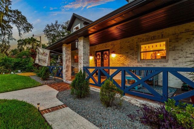 exterior entry at dusk featuring covered porch and brick siding