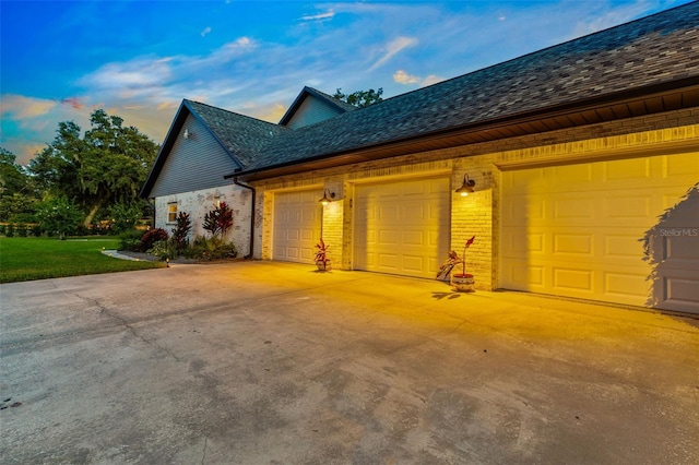 view of side of home featuring a garage, driveway, brick siding, and a lawn