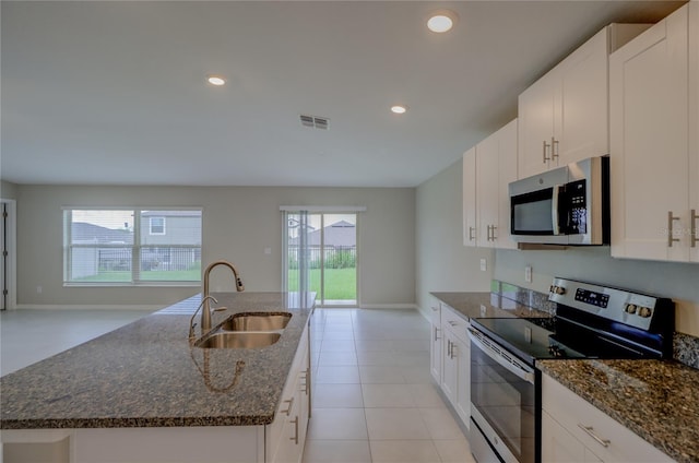 kitchen with a center island with sink, stainless steel appliances, sink, dark stone countertops, and white cabinets