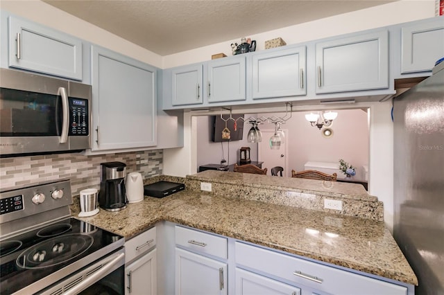 kitchen featuring white cabinetry, stainless steel appliances, light stone counters, an inviting chandelier, and decorative backsplash