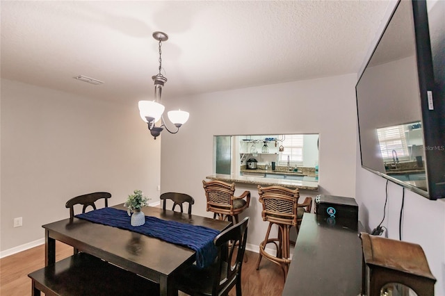 dining space with a textured ceiling, wood-type flooring, and a notable chandelier