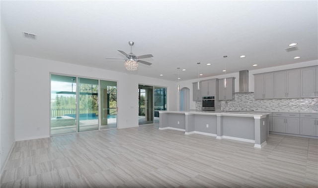 kitchen with an island with sink, pendant lighting, wall chimney range hood, stainless steel oven, and a kitchen breakfast bar