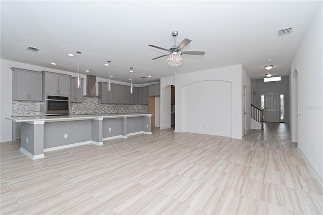 kitchen with gray cabinetry, stainless steel oven, wall chimney exhaust hood, and a spacious island