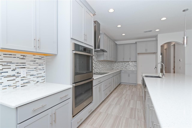 kitchen featuring gray cabinetry, wall chimney exhaust hood, sink, pendant lighting, and backsplash