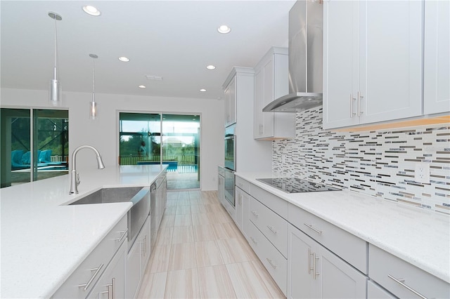 kitchen with stainless steel appliances, pendant lighting, wall chimney range hood, white cabinetry, and backsplash