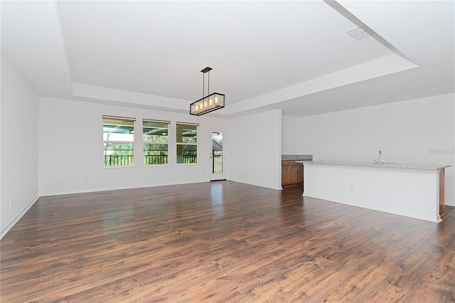 unfurnished living room with a raised ceiling and dark hardwood / wood-style flooring