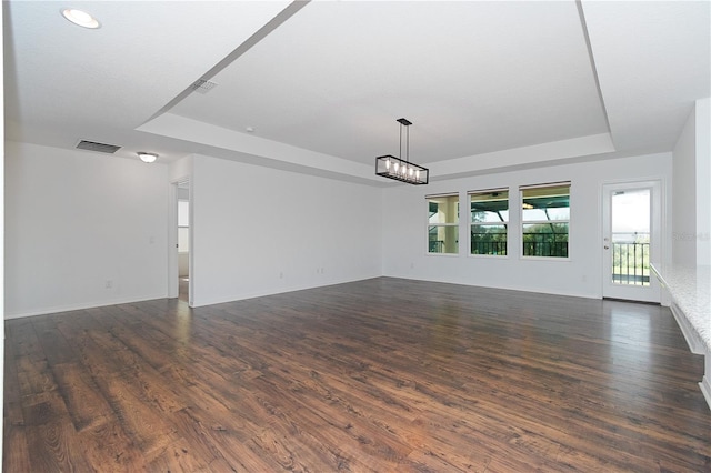 unfurnished room featuring an inviting chandelier, a tray ceiling, and dark wood-type flooring