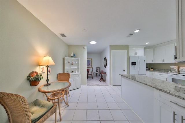 kitchen featuring light tile patterned floors, white appliances, light stone countertops, and white cabinets