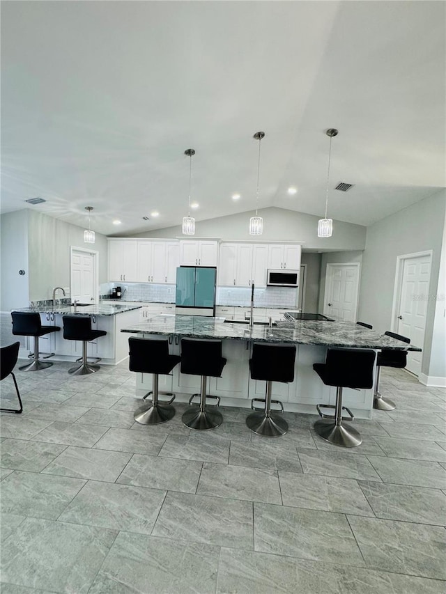 kitchen featuring vaulted ceiling, stainless steel fridge, a spacious island, a kitchen bar, and white cabinetry