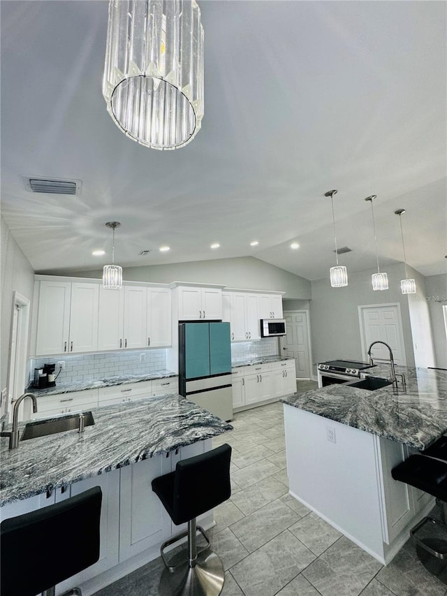 kitchen featuring dark stone countertops, vaulted ceiling, decorative light fixtures, and stainless steel appliances