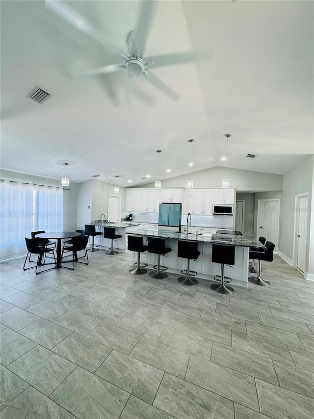 interior space featuring backsplash, stainless steel refrigerator, white cabinetry, a large island, and ceiling fan