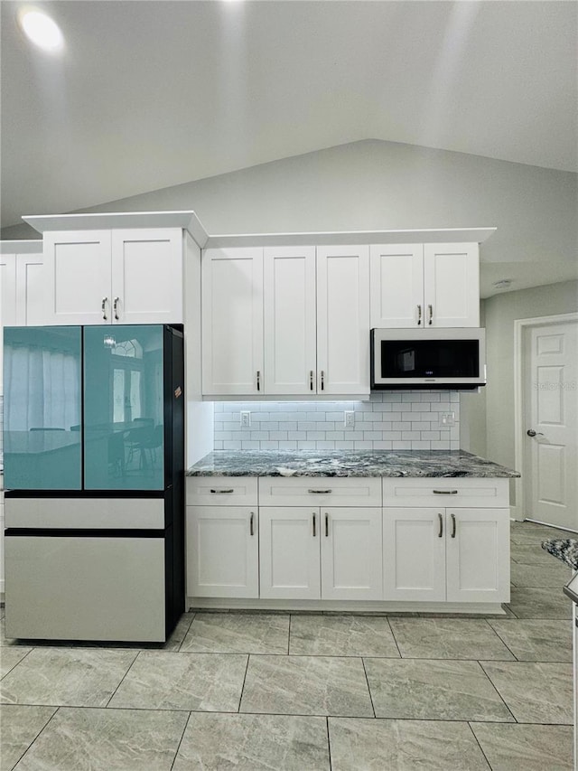 kitchen with stone countertops, white cabinetry, lofted ceiling, fridge, and decorative backsplash