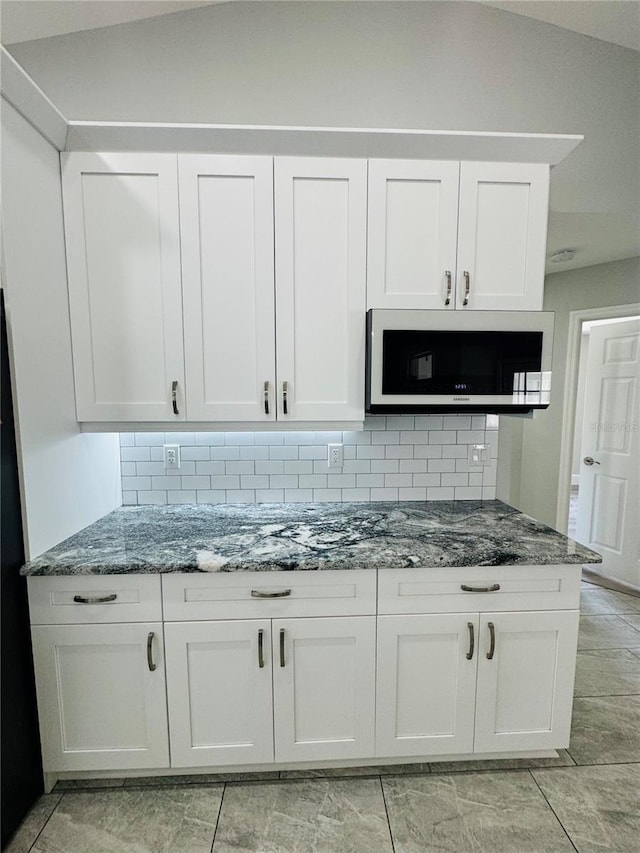 kitchen with lofted ceiling, backsplash, stone counters, and white cabinets