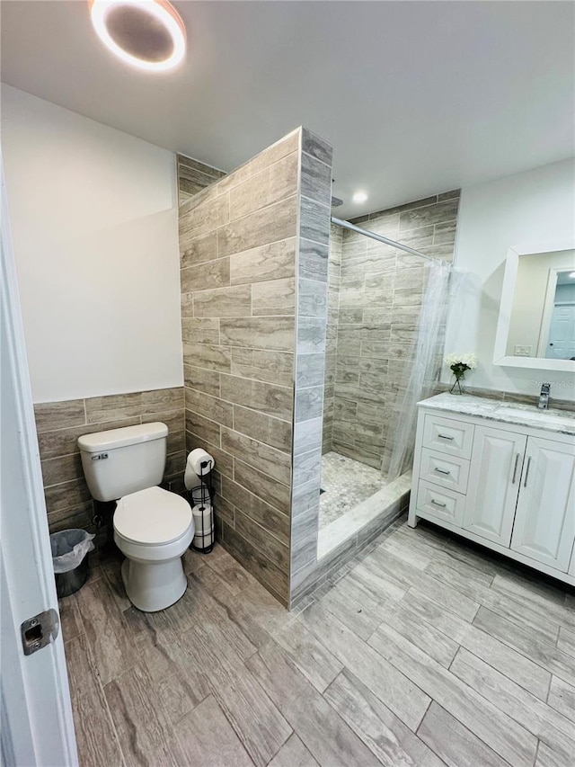 bathroom featuring vanity, hardwood / wood-style floors, a tile shower, tile walls, and toilet