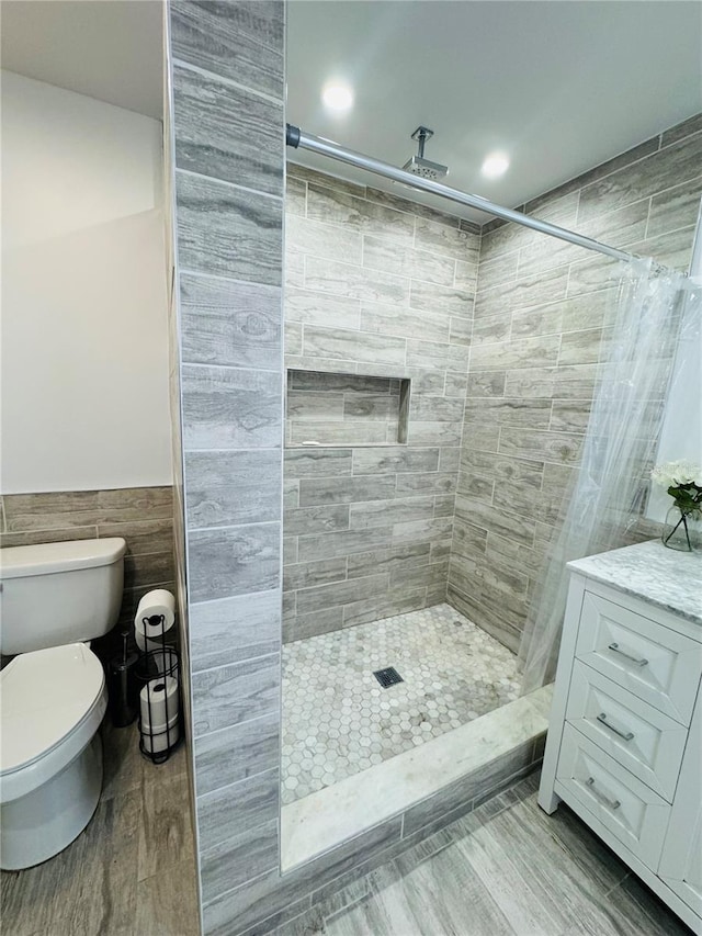 bathroom with vanity, wood-type flooring, a tile shower, tile walls, and toilet