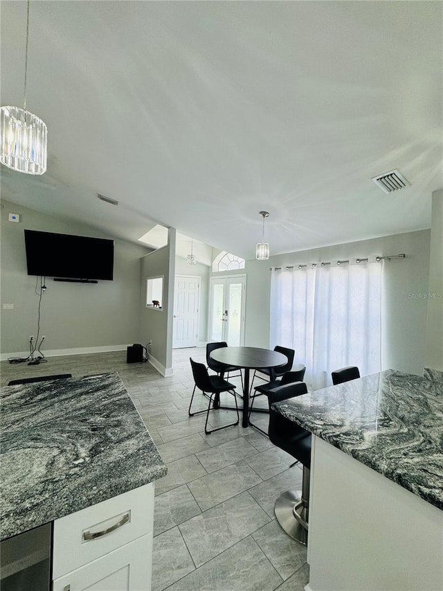 kitchen with dark stone countertops, lofted ceiling, white cabinets, and hanging light fixtures